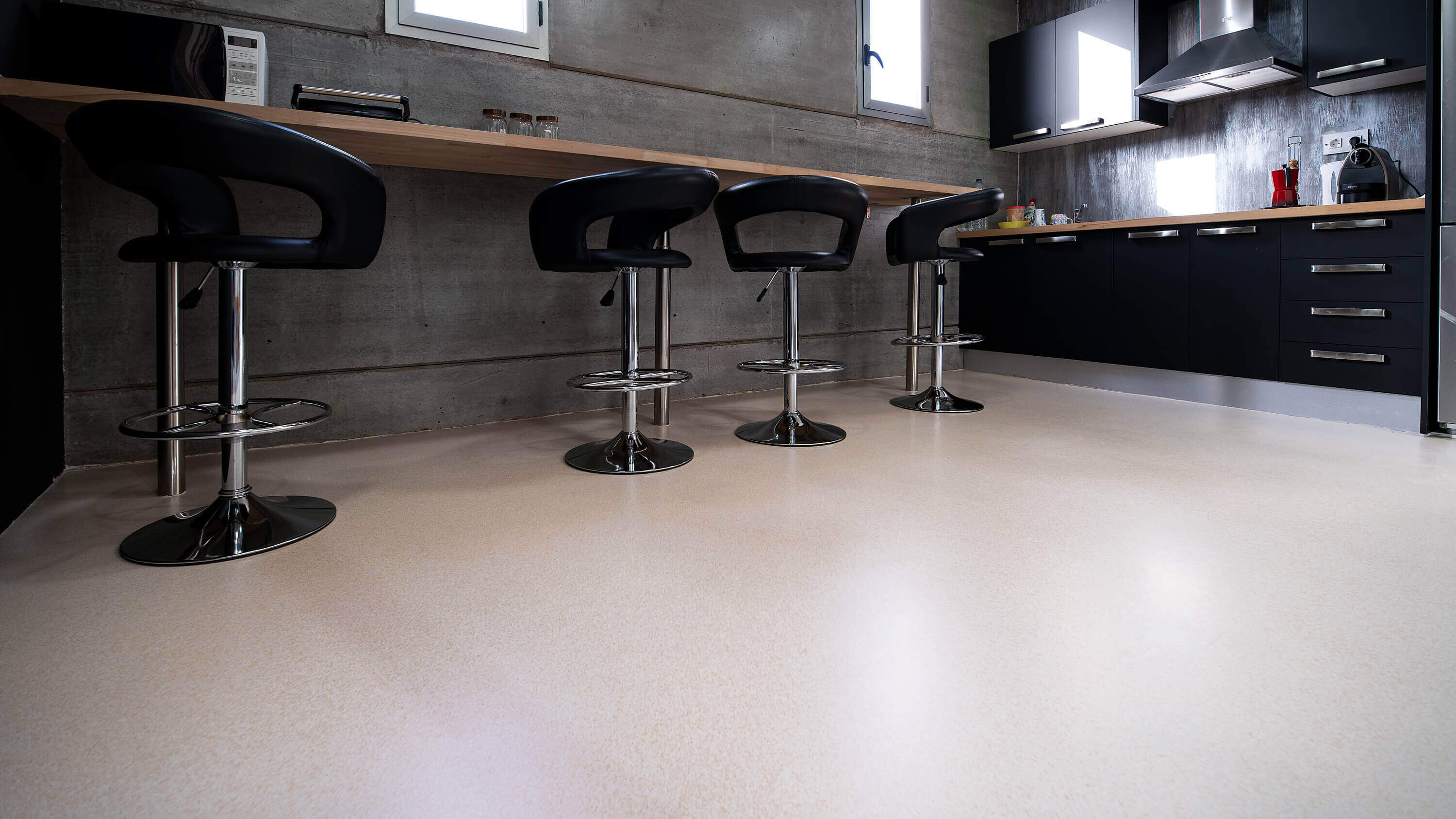 Light-coloured seamless flooring in a kitchen with a counter and stools